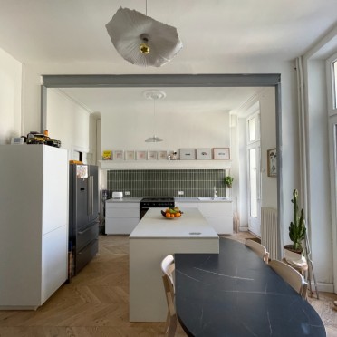 Cuisine ouverte design avec îlot blanc, table noire en marbre, parquet bois clair et électroménager intégré